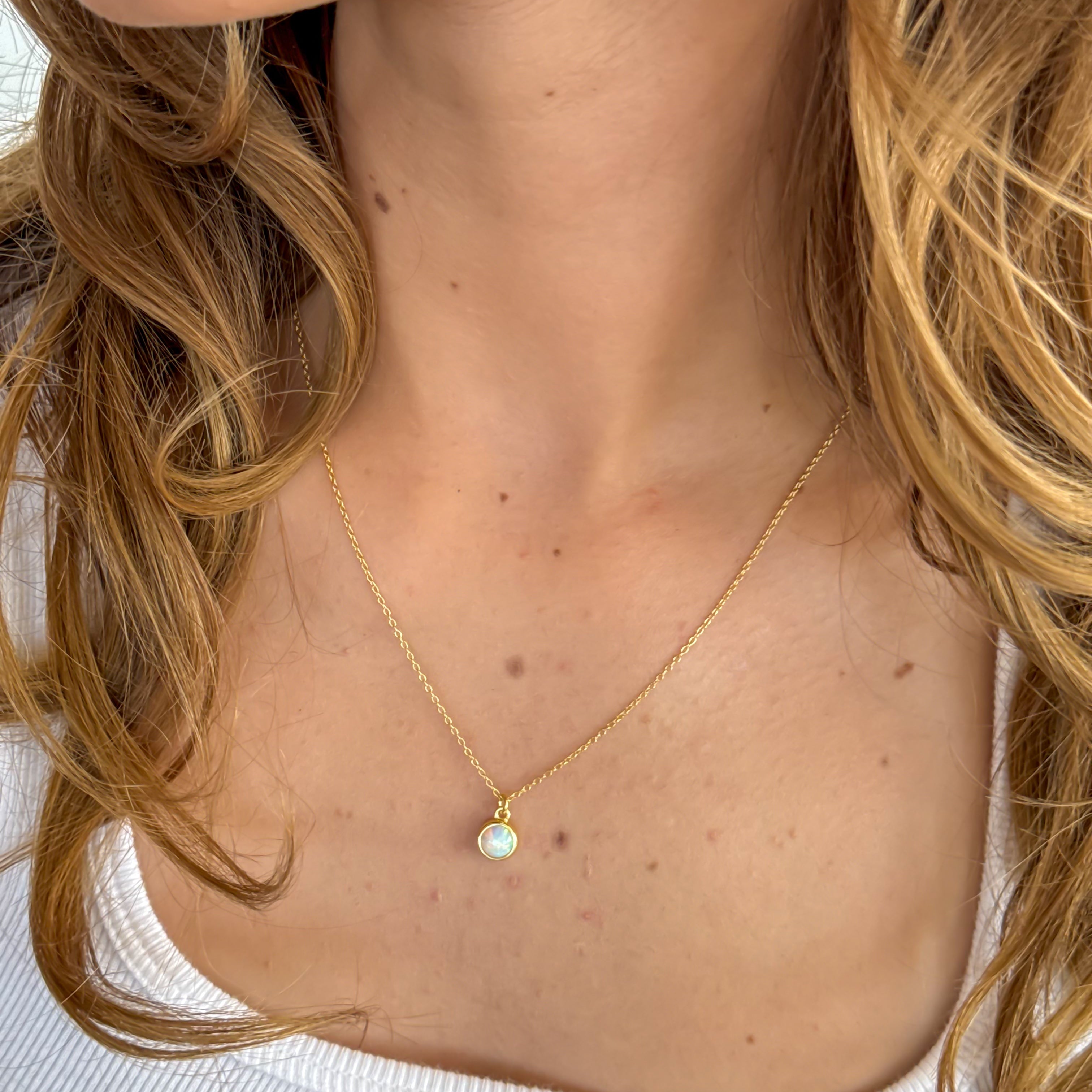Close-up of a person wearing a gold necklace with a pendant, focusing on the neck and shoulders.