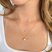 Gold necklace with a pearl pendant worn by a person