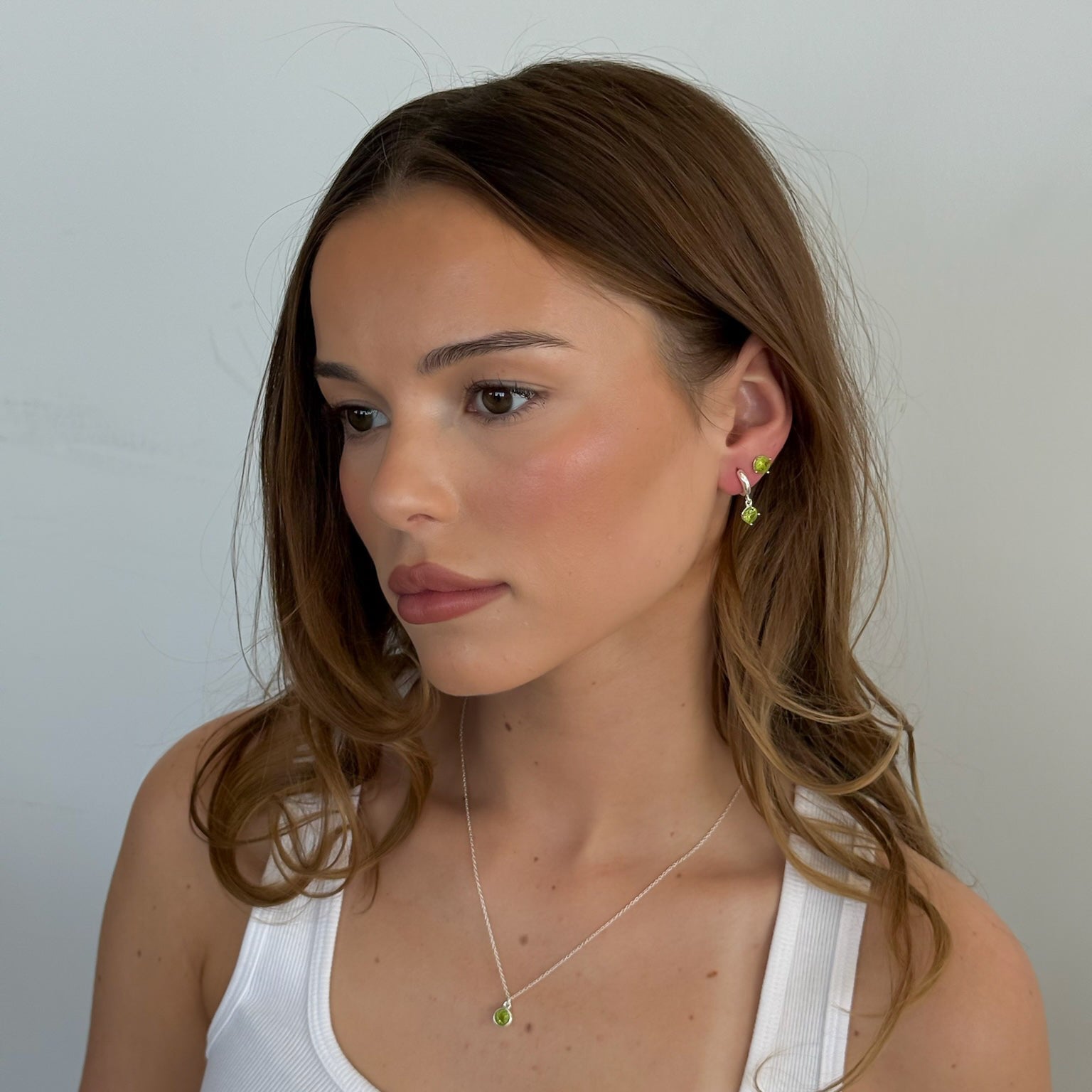 Woman wearing a necklace and earrings against a plain background