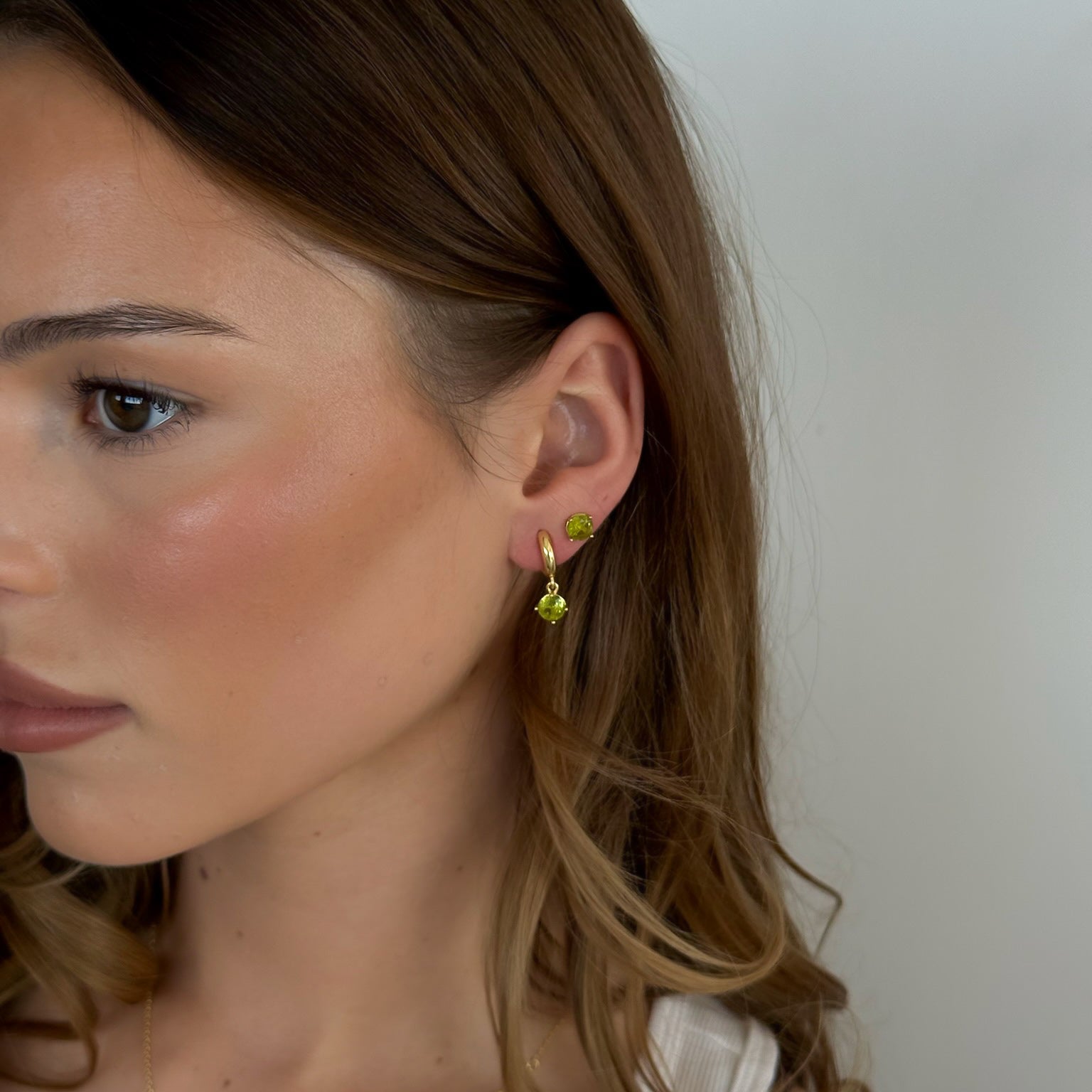 Close-up of a woman wearing small green earrings against a neutral background