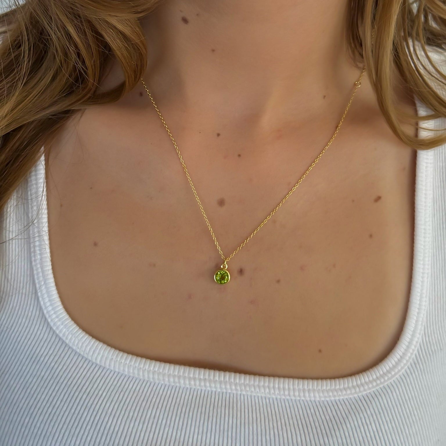 Gold necklace with a green pendant worn by a person against a white background