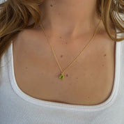 Gold necklace with a green pendant worn by a person against a white background