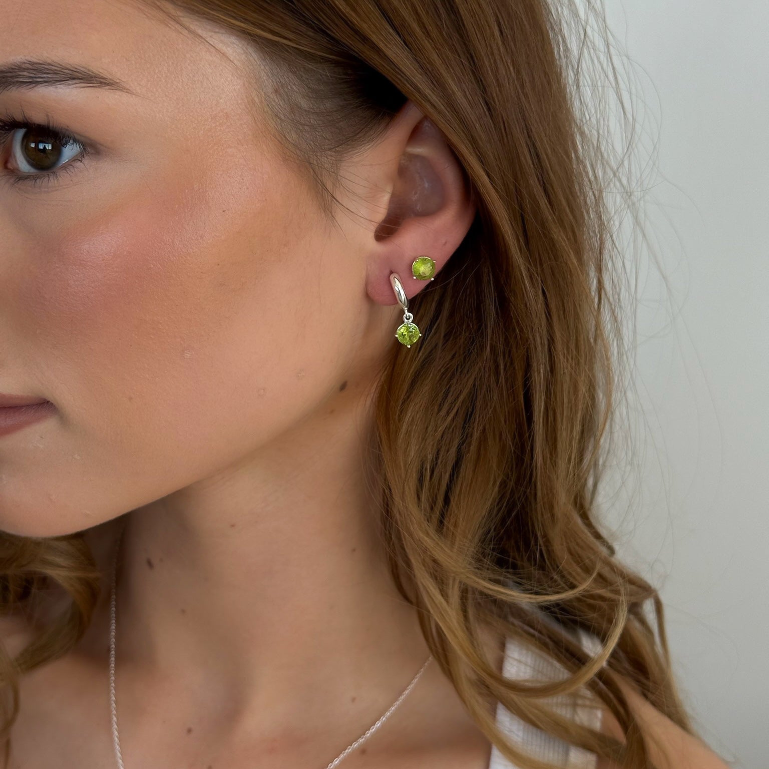 Close-up of a woman wearing a green earring with a plain background