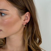 Close-up of a woman wearing gold hoop earrings with red gemstones against a neutral background